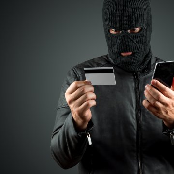 Comparison Identity Guard LifeLock identity theft protection services id thief with stolen credit card and smartphone in hand and black mask on face